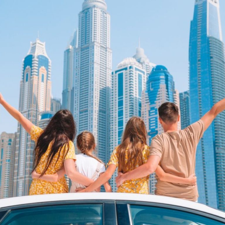 A family, including parents and two daughters, standing on a car in front of a building in Dubai.